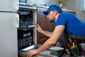 %Title% | 3 Mountains Home Services A 3 Mountains Home Services technician in a blue uniform inspects a dishwasher, tool in hand, providing expert kitchen service.
