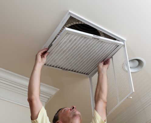 A 3 Mountains Home Services technician stands on the floor, replacing an air filter in a ceiling vent of a customer's home.