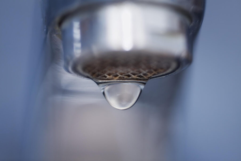A close up picture of a faucet with one drop almost ready to fall.