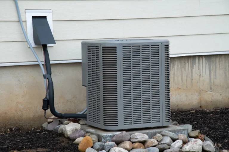 A 3 Mountains Home Services outdoor AC unit sits on a concrete pad by a home, neatly surrounded by rocks and mulch.